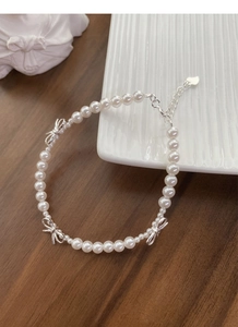 Détail du bracelet en perles et nœud argenté avec breloque cœur sur bois