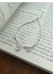 Detailaufnahme des S925 Silberarmbands mit Herzanhänger und Mondstein auf Buch