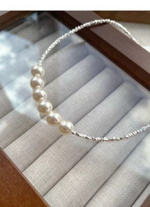 Detailed macro of six round cream pearls on a textured silver chain necklace