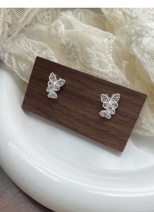 Macro detail of silver butterfly earrings with filigree wings on wood and ceramic