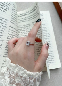 Macro detail of a sparkling square zircon silver ring worn while reading an elegant book