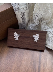 Detailed macro view of S925 silver hollow filigree butterfly stud earrings on wooden display