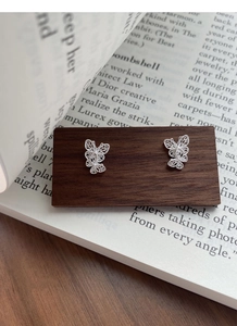 Macro detail of silver butterfly earrings with delicate filigree pattern on dark wood