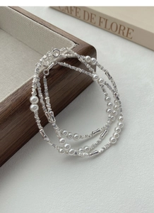 Detail of stacked S925 silver beaded bracelets with white pearls on a rustic wooden tray