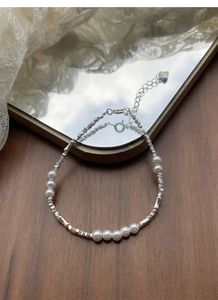 Detailed shot of S925 silver pearl bracelet with heart charm on a rustic wooden surface