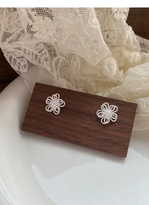Gros plan sur les boucles d'oreilles fleurs évidées en argent S925 sur support en bois