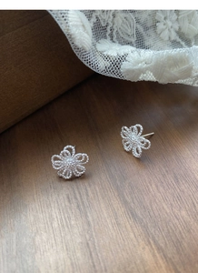 Vue macro des boucles d'oreilles fleuries argentées évidées avec texture fine sur bois