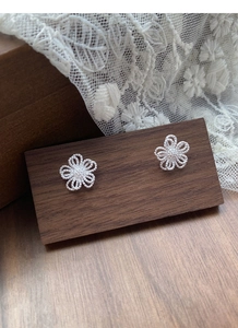 Vue macro des boucles d'oreilles fleurs ajourées en argent S925 sur support en bois