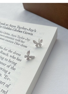Detailed view of silver butterfly stud earrings with fine brushed texture on a book