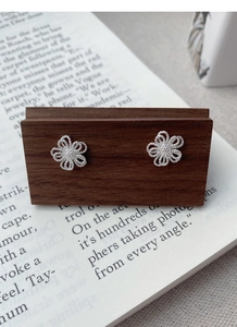 Gros plan sur des boucles d'oreilles fleurs évidées en argent sur un support en bois