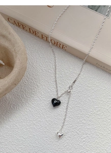 Detail of S925 silver necklace with black heart tassel on a Parisian cafe style book
