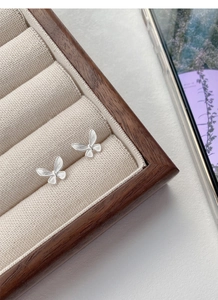 Macro view of butterfly earrings featuring a brushed silver finish on a wooden display