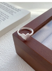 Macro detail of silver origami heart ring with brushed finish on a wood display box