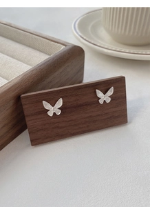 Detailed close-up of S925 sterling silver butterfly stud earrings on wood display