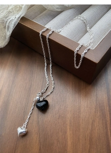 Detail view of S925 sterling silver Y-shaped necklace with black heart pendant on wood