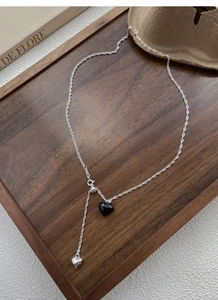 Close-up of S925 silver Y-shaped necklace with black heart and tassel on a wood tray