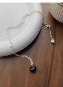Macro shot of S925 silver necklace with black heart pendant and tassel on wooden surface