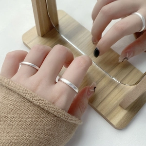 Bagues minimalistes en argent massif S999 mat sur main avec un fond de miroir en bois rustique