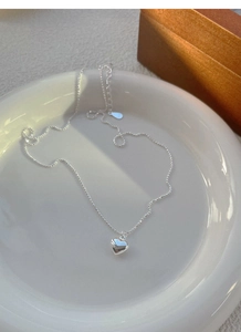Close-up of S925 sterling silver heart necklace with bead chain on white ceramic tray