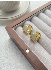 Primo piano di orecchini d'oro geometrici irregolari in una scatola di legno per gioielli
