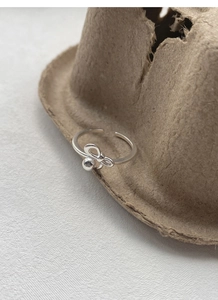 Close-up of S925 sterling silver bow ring with bead detail on a textured paper backdrop