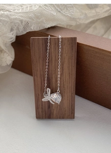 Macro detail of S925 silver bow heart pendant necklace on elegant lace and wood