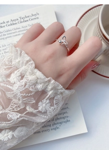 Detailed view of an S925 silver bow ring worn elegantly against a vintage book background