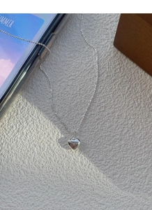 Detail of S925 sterling silver heart pendant necklace on a textured white background