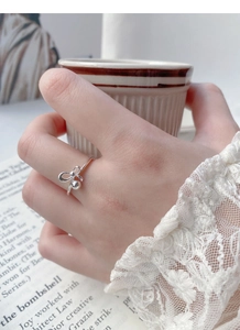 Detail of S925 sterling silver bow ring with dangling bead worn in a lifestyle setting