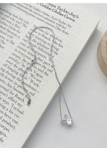 Close-up of S925 sterling silver bow heart pendant necklace on an open book