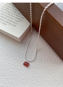 Macro shot of silver beaded necklace featuring a rectangular red-brown gemstone pendant