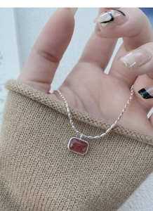 Macro shot of S925 silver necklace with strawberry crystal pendant against a knit sweater