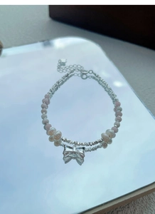 Detail of pink beads and freshwater pearl bracelet with a silver bow charm pendant