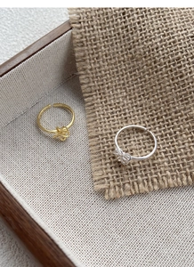 Macro shot of silver and gold open flower rings on beige textured fabric and wood