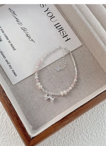 Detail of S925 silver bracelet with pink beads, pearls and a silver bow charm in a wooden tray