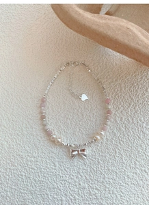 Detail of pink stone beads and pearl bracelet with silver bow pendant and heart tag