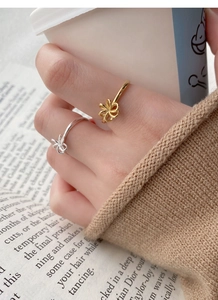 Detail of silver and gold hollow flower rings worn with a knit sweater and coffee cup