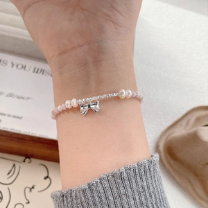 S925 silver pink bead and freshwater pearl bracelet with a metallic bow charm on wrist