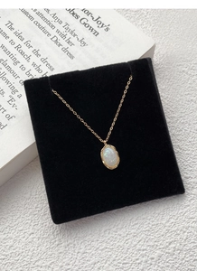 Detailed macro view of an oval white opal pendant on a fine gold necklace chain