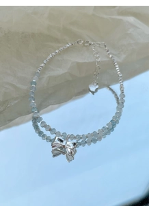 Macro detail of S925 silver bow charm and aquamarine beaded bracelet with heart tag