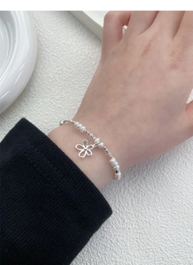 Detailansicht des Süßwasserperlenarmbands mit silbernem Blumenanhänger am Handgelenk