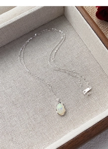 Macro view of 925 sterling silver chain with an oval opal pendant on linen display