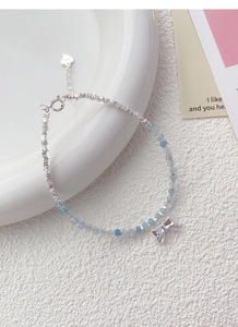Detailed close-up of S925 sterling silver bow charm and aquamarine beaded bracelet