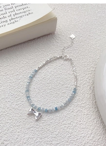 Detailed close-up of a silver bow pendant and light blue beads on a delicate S925 bracelet