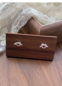 Detailed macro view of S925 sterling silver knot stud earrings on a dark walnut display