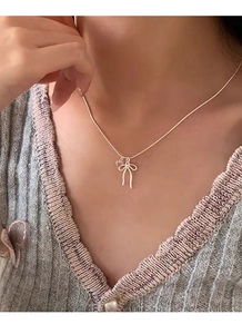 Dettaglio di una collana dorata con ciondolo a fiocco e cuore su catena a serpente