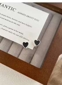 Detailed macro view of black enamel heart earrings with silver beaded edges in a wooden box
