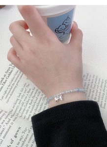 Detail of S925 silver bow charm on a blue beaded bracelet worn against a black sleeve