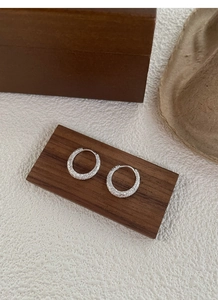 Macro shot of silver hoops featuring a textured crushed silver finish on a wooden display