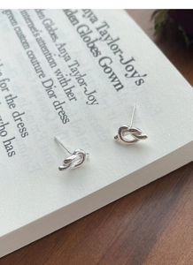 Detailed close-up of S925 sterling silver knot stud earrings on a vintage book page